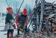 Inga Mari Hætta cutting firewood with a chain saw while her daughter Inga Ellen Kristine Hætta looks on (Northern Norway in 1974). Photo: Hugh Beach.